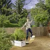 A young person is balancing on a wooden board on a deck, surrounded by greenery and a bamboo fence. Produktbild-Vorschau