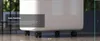 A white air conditioner unit with wheels is shown on a textured floor, with a dark overlay box containing text on the left. Produktbild-Vorschau