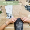 Hands are shown assembling or decorating a black paper bag, surrounded by other decorative paper bags and crafting supplies. Náhľad obrázku produktu