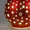 A close-up of a red decorative glass lamp with cut-out star shapes, illuminated from within. Produktbild-Vorschau
