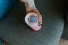 A person's hand holding a pink and white thermos cup with a blue lid. Náhled obrázku produktu
