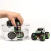 A child's hand is shown dipping a toy monster truck into a glass bowl of water, with another toy monster truck visible to the right. Voir les images du produit