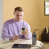 A man is sitting at a table, charging his phone and tablet with a power bank. Produktbild-Vorschau