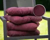 A stack of four purple seat cushions on a dark gray chair outdoors. Produktbild-Vorschau
