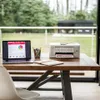 A printer and laptop are set up on a wooden table in front of a large window with a view of a garden. Podgląd zdjęcia produktu