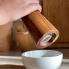 A hand is holding a wooden pepper grinder over a white bowl. Náhled obrázku produktu