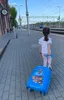 A young girl is pulling a blue Paw Patrol suitcase on a train station platform. Náhľad obrázku produktu