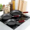 A set of cast iron frying pans on a black induction stovetop, with jars of pasta and other kitchen items in the background. Voir les images du produit