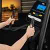 A person's hands are gripping the handlebars of an elliptical trainer, with the console visible in the background. Produktbild-Vorschau