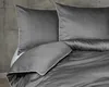 A close-up view of gray bedding, including pillows and a duvet, against a concrete wall. Náhled obrázku produktu