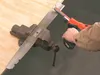 A person is using a Black & Decker power file to sharpen a metal blade held in a vise. Náhľad obrázku produktu
