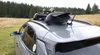 A car with skis and snowboards mounted on the roof rack, parked in a grassy field with a forest in the background. Produktbild-Vorschau