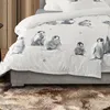 A close-up view of a bed with penguin-themed bedding, showing the texture and pattern of the duvet cover and a fluffy rug in the foreground. Produktbild-Vorschau