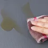 A hand is wiping a spill on a textured gray surface with a brown and pink striped cloth. Náhled obrázku produktu