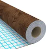 A roll of wood-grain patterned adhesive film is shown on a white background with a grid pattern underneath. Náhľad obrázku produktu