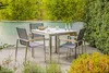 An outdoor dining set with a table and four chairs on a patio, surrounded by greenery. Produktbild-Vorschau