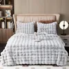 A plush blanket and pillows are neatly arranged on a bed, with a bedside table and lamp visible. Náhled obrázku produktu
