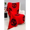 A red fleece blanket with the Manchester United logo is draped over a chair. Náhľad obrázku produktu