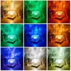 A collage of nine images, each showing a cube-shaped lamp projecting colorful light patterns onto a background. The lamps are shown in different colored lighting environments: yellow/orange, green, blue, and white. Produktbild-Vorschau