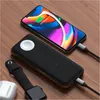 A Satechi Quatro Wireless Power Bank is shown charging an iPhone and an Apple Watch, with AirPods nearby, on a wooden surface. Produktbild-Vorschau