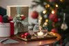 A festive Christmas scene with gifts, a lit candle in a glass holder, and a decorated Christmas tree in the background. Produktbild-Vorschau