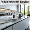 A modern kitchen countertop with two electric kettles, one white and one black, displayed prominently. The background shows sleek kitchen cabinetry and a window with a view of greenery. Produktbild-Vorschau