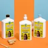 Three bottles of hair product are displayed on an orange and blue background, with ginger root and a wooden spoon in the foreground. Náhled obrázku produktu