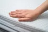 A hand is resting on a white quilted mattress topper. Náhľad obrázku produktu