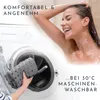 A woman is showering while a bath mat is being placed into a washing machine. Produktbild-Vorschau
