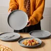A person holding a plate, with other plates and food on a table. Produktbild-Vorschau