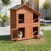 Two rabbits are in front of a wooden, multi-level rabbit hutch in a grassy yard. Anteprima dell’immagine prodotto