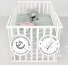 A white crib with a green patterned mattress, a gray teddy bear, and a pink star pillow inside. Náhled obrázku produktu