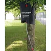 A black camp shower bag is hanging from a tree branch, with a clear tube extending downwards. Produktbild-Vorschau