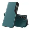 A teal flip case for a smartphone is shown, standing upright and open to reveal the phone's camera module. Náhled obrázku produktu