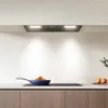 A modern kitchen scene featuring a sleek range hood, a frying pan with food on a stovetop, and two oranges. Anteprima dell’immagine prodotto
