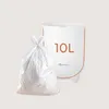 A white diaper pail with '10L' printed on it and a tied-off white trash bag in front of it, against a light beige background. Produktbild-Vorschau