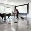 A man is vacuuming a modern office or meeting room with a large projector screen in the background. Produktbild-Vorschau