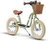 A green Puky balance bike with a brown seat and handlebars, and a wicker basket on the front, is shown against a white background. Náhled obrázku produktu