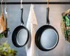 Two frying pans hanging on a rack in a kitchen, with a dishtowel and other kitchen utensils also hanging. Produktbild-Vorschau