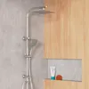 A modern shower system with a rain shower head and a handheld shower head, mounted on a wall with a concrete texture and a wooden accent panel. A small shelf in the wooden panel holds a tube of lotion and a loofah. Produktbild-Vorschau