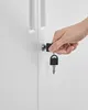 A hand is inserting a key into the lock of a white cabinet door. Náhled obrázku produktu