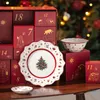 A Christmas-themed advent calendar with plates and bowls, set against a blurred Christmas tree background. Produktbild-Vorschau