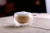 A close-up shot of a cappuccino in a double-walled glass mug, placed on a textured fabric surface. Produktbild-Vorschau
