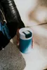A person's hand holding a blue and white Kambukka thermobottle. Náhled obrázku produktu