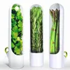 Three clear containers with white bases, each holding fresh produce. The leftmost contains cilantro, the middle contains rosemary, and the rightmost contains asparagus. Each container has a small green loop handle on its side. Produktbild-Vorschau