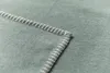 A close-up of a corner of a green blanket with white stitching. Produktbild-Vorschau