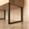 A close-up view of black metal furniture legs supporting a wooden cabinet, set against a tiled wall and a reflective floor. Produktbild-Vorschau