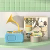 A blue toy gramophone with a yellow horn sits on a light green shelf, next to a box with product images and a stack of colorful discs. Náhľad obrázku produktu
