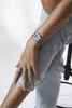 A person wearing a watch and jeans, sitting down. Produktbild-Vorschau