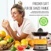 A woman holding a glass of juice next to a collection of citrus fruits and a juicer. Produktbild-Vorschau
